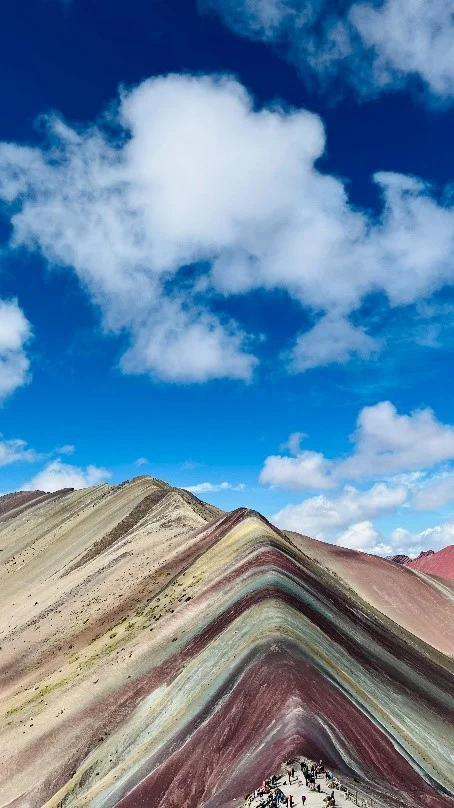 Cumbre de la Montaña de Siete Colores o Vinicunca con sus franjas minerales bajo un cielo azul con nubes
