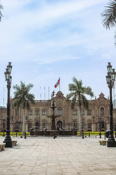 Fachada principal del Palacio de Gobierno con la bandera de Perú, la pileta de bronce y palmeras en la Plaza Mayor de Lima
