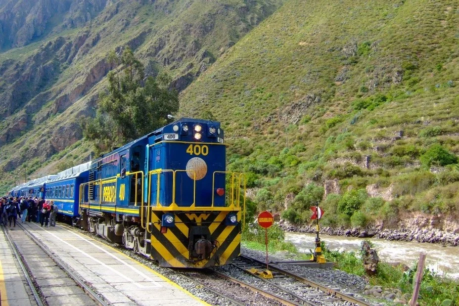 Tren azul de PeruRail con el número 400 detenido junto al río Urubamba y rodeado de montañas en el Valle Sagrado